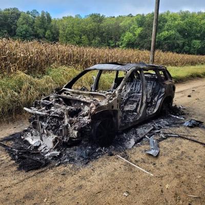 A car completely burned up in a field. Debris scattered near the burned car.