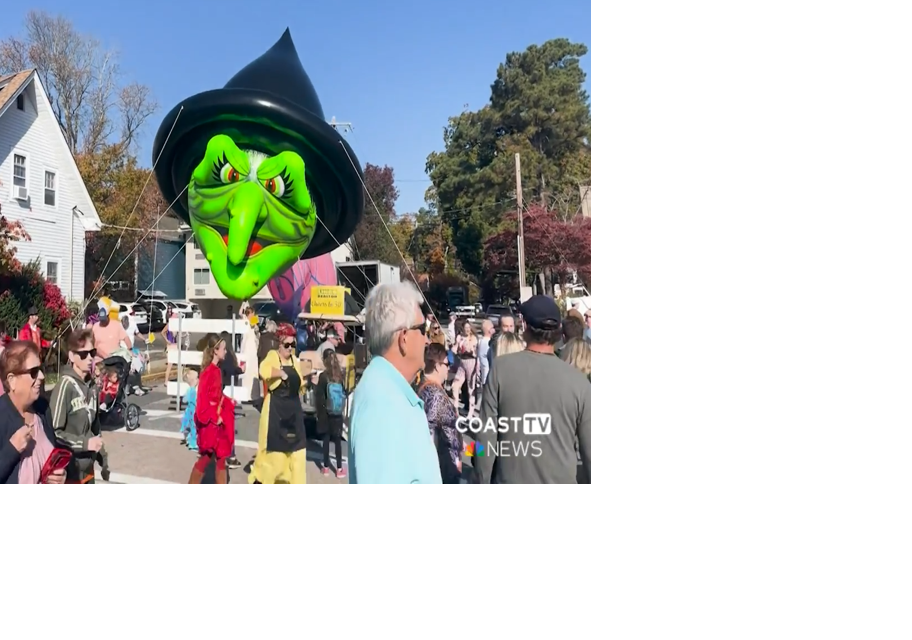 A green witch balloon is held in the air during a parade.