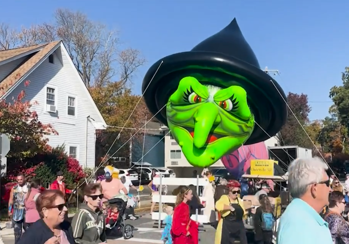 A green witch balloon is held in the air during a parade.