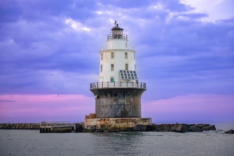 A sunset photograph of the Harbor of Refuge Lighthouse standing off Cape Henlopen State Park against a dramatic purple-blue sky.