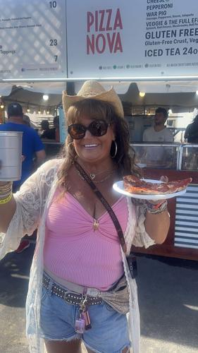 A woman holds up her large slice of pizza in front of the food vendors.