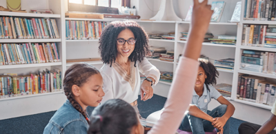 Woman in room with white shelves covered in books and three children raising their hands