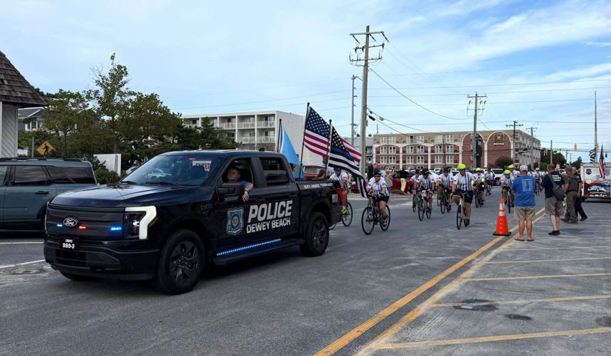 Bicyclists following behind a Dewey Beach police car.