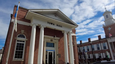 A town hall government building on a sunny day with a flagpole in the front. 