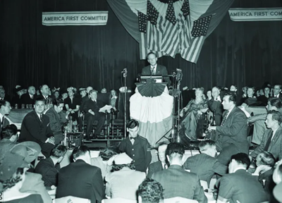 a man addresses a crowd under american flags in a black and white image 
