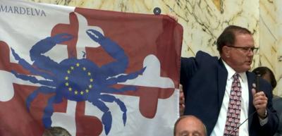 A man holds up a flag with a blue crab and a red and white background.