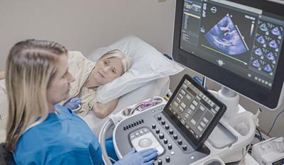 A female medical professional is caring for a female patient laying in a hospital bed with an ultrasound displayed on the screen.