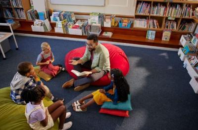 Children sitting around a teacher on the floor as he reads to them.