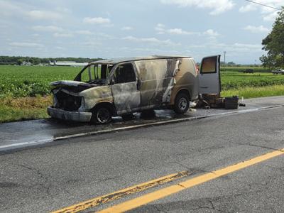 A burned van sits on the side of a road.