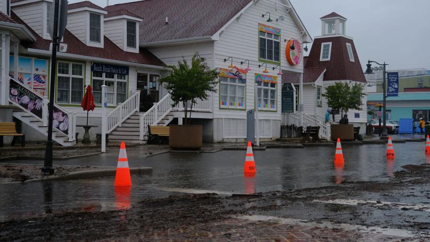 Parking spaces covered with water in front of a building are blocked off with orange traffic cones. The road is covered with dirt and mulch.
