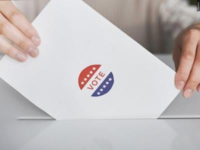 A piece of paper that says "vote" being put into a ballot box.