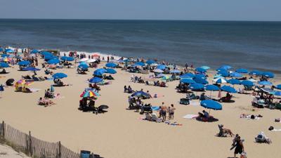 Beachgoers gather under umbrellas and cool off in the ocean in Rehoboth Beach during a hot day.