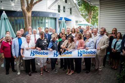 A crowd cuts a ribbon with the name "Beebe Healthcare" on it.