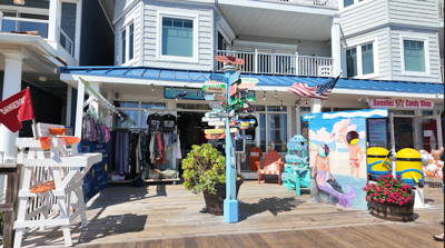 A multi-directional sign in front of a store on a boardwalk with a blue canopy.