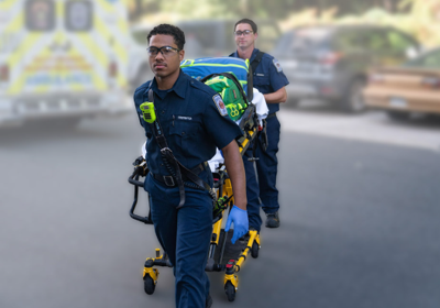 Two EMS crew members wheeling a gurney with an ambulance in the background