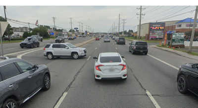 Cars drive on a three lane highway past businesses.