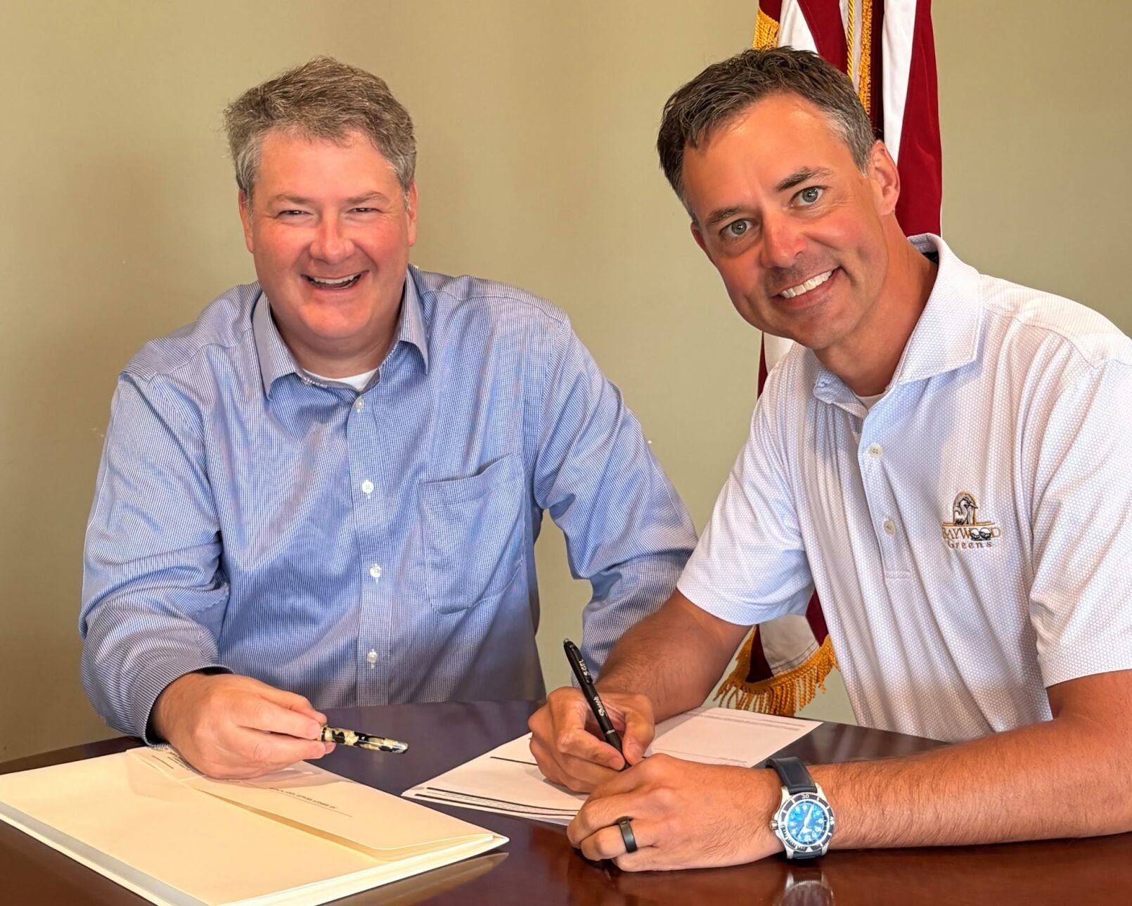 two men smiling signing papers