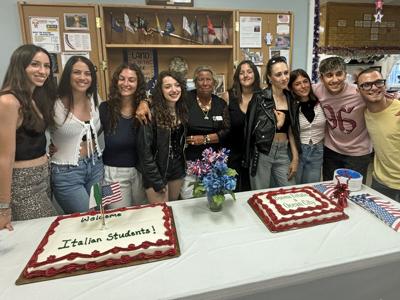 Ten people posing in front of two cakes with red icing.