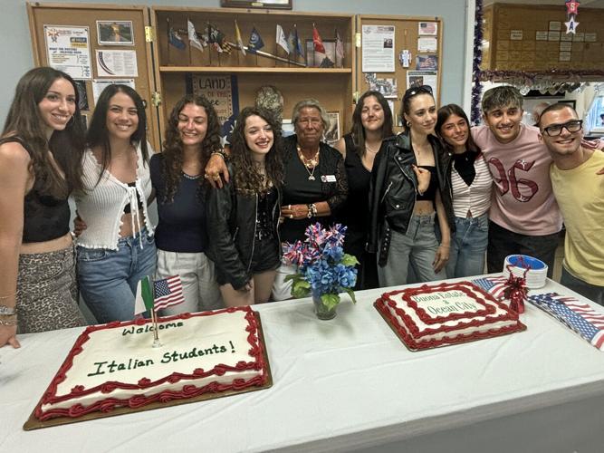 Ten people posing in front of two cakes with red icing.