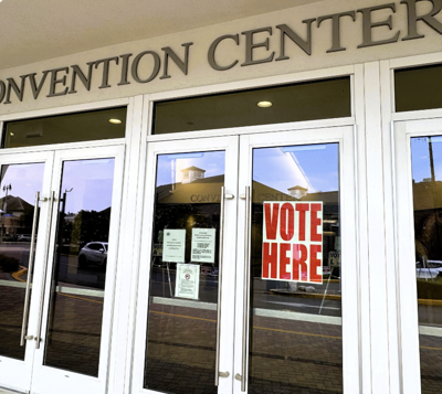 Brown building with white doors and a sign that says "vote here"