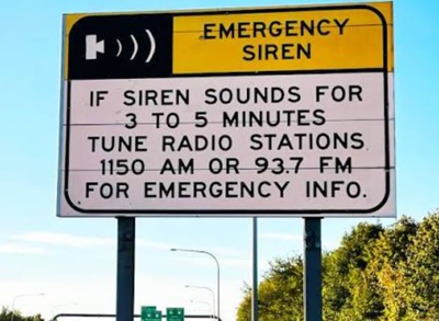 The Emergency Siren sign on DE Route 1 reading if a siren sounds for 3 to 5 minutes tune radio stations 1150 AM or 93.7 FM for emergency information.