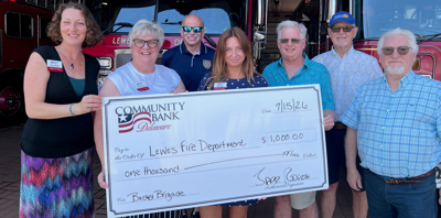 A large check is being presented by the Community Bank Delaware for one thousand dollars. a group of adults pose for a photo. 