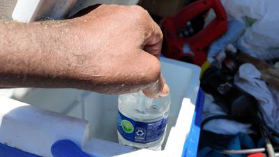 An outdoor worker pulls a water bottle from a cooler.