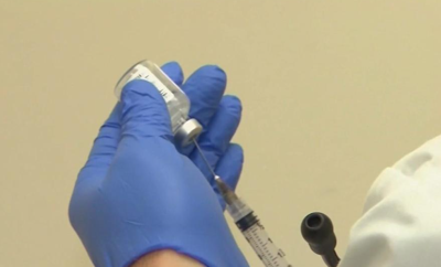 A syringe getting filled with a chemical held by a blue latex glove.