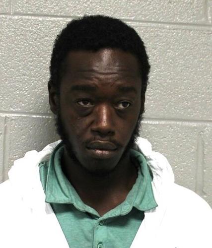 A mugshot of the suspect against a white wall. He is black and wearing a green polo and white hooded jacket.