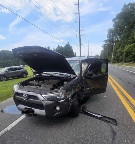 A Black SUV on the side of the road with the hood and driver's door open and airbags deployed. There is damage to the driver's side of the vehicle towards the front.