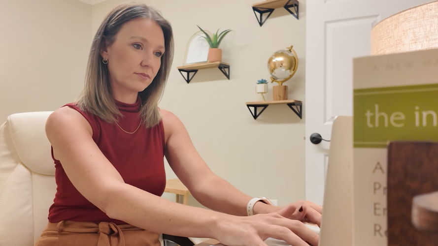 A woman in a red shirt typing at a computer. 
