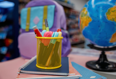 school supplies sit on a desk, a globe and backpack are in the background 