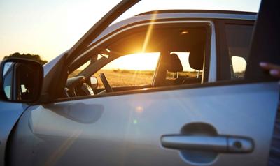 A grey car with the suns rays shining through the drivers side window. 