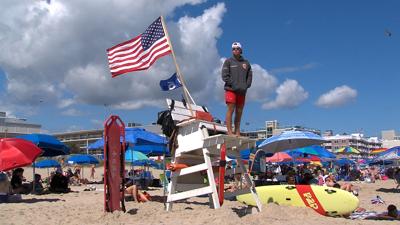 A Rehoboth Beach lifeguard standing on a chair looking out over the beach.
