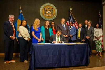 Governor Matt Meyer sitting at a table with a group of people signing the new law. 