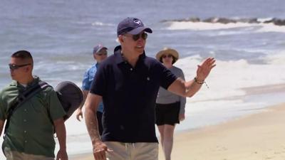 Former President Joe Biden walking on a Delaware beach, waving.