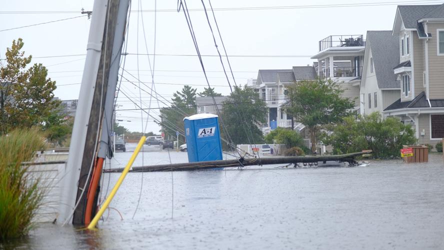 Power lines and a pole are laying down in front of a blue portapotty on a flooded street.