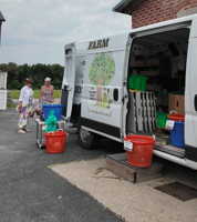 A white van is set up in a parking lot with bins of produce outside of it.