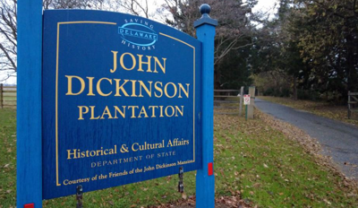 The sign at the John Dickinson Plantation's 450 acre property. It has a blue background with yellow lettering reading John Dickinson Plantation Historic & Cultural Affairs.