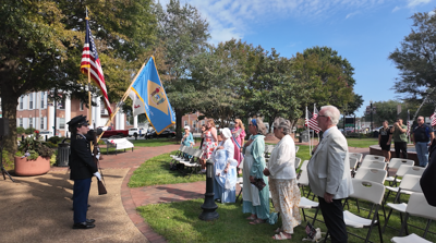 People standing in front of white chairs pledging the Americana and Delawarean flag.
