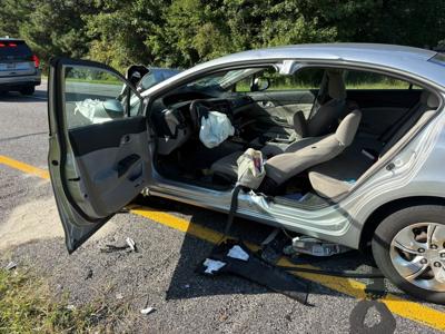 A silver colored car seriously damaged in a crash. The left passenger door is torn off and the air bag is deployed underneath the steering wheel.