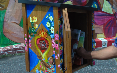 A book is pulled out of a wooden cabinet painted with flowers and a book.