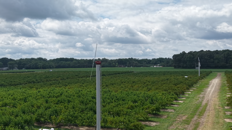 A tall pole with a propeller on the top towers over a farm.