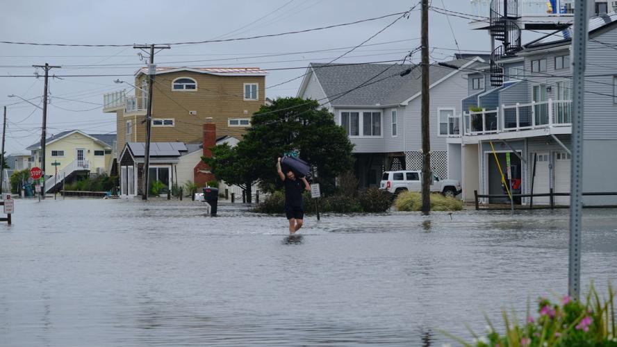 A man carries a suitcase through water that is up to his knees.