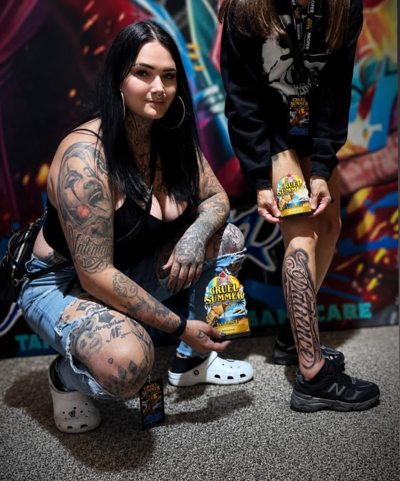 a woman with tattoos, ripped jeans, white crocs and black hair poses next to the leg of a person that has been tattooed, the tattoo is on their leg, it reads 'patience' 