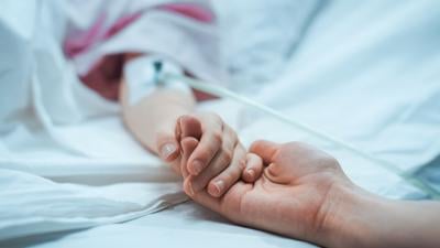 Recovering Little Child Lying in the Hospital Bed Sleeping, Mother Holds Her Hand Comforting. Focus on the Hands. Emotional Family Moment.