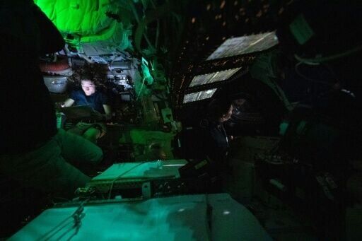 This handout picture by an Artemis II crew member provided by NASA shows Christina Koch illuminated by a screen inside the darkened Orion spacecraft as Jeremy Hansen (R) peers out of one of Orion's windows