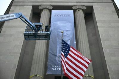 Workers on an aerial lift watch after installing a new banner featuring an image of US President Donald Trump on the facade of the US Department of Justice headquarters building in Washington, DC