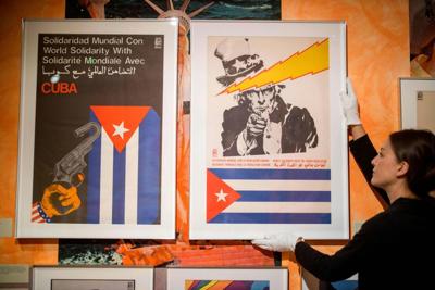 A gallery worker works with an artwork titled 'World Solidarity with the Cuban Revolution' alongside other posters by the Organization of Solidarity with the Peoples of Africa, Asia, and Latin America.