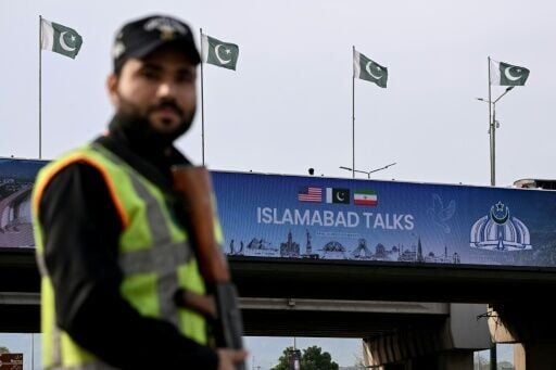 A policeman stands guard in front of a digital screen displaying news of US–Iran peace talks along a road in Pakistan's capital Islamabad